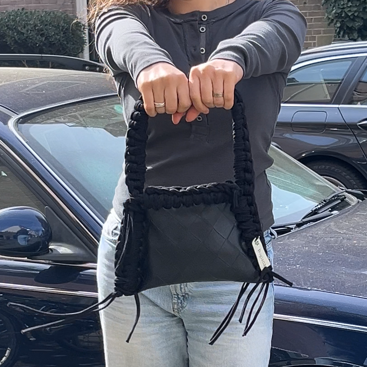 Person holding a black handbag with a car in the background