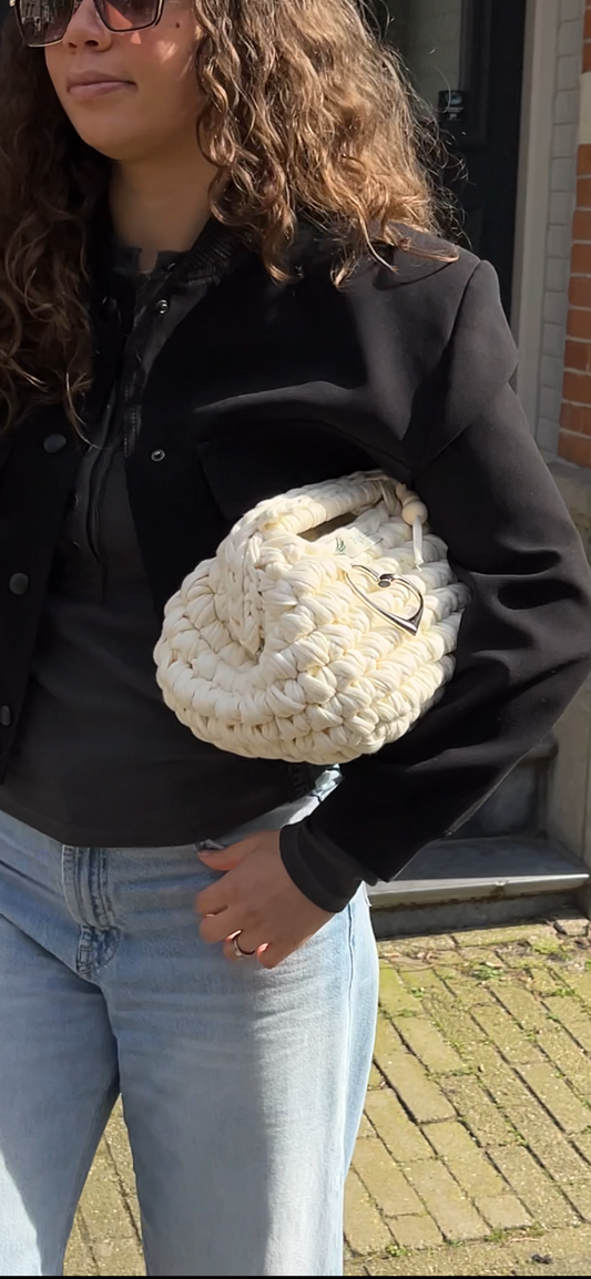 Person holding a textured white bag outdoors with a brick building in the background