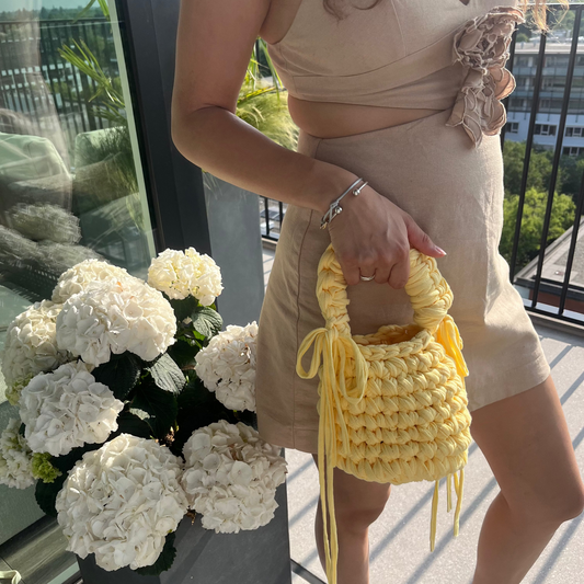 Woman holding a yellow handbag next to a flower arrangement indoors