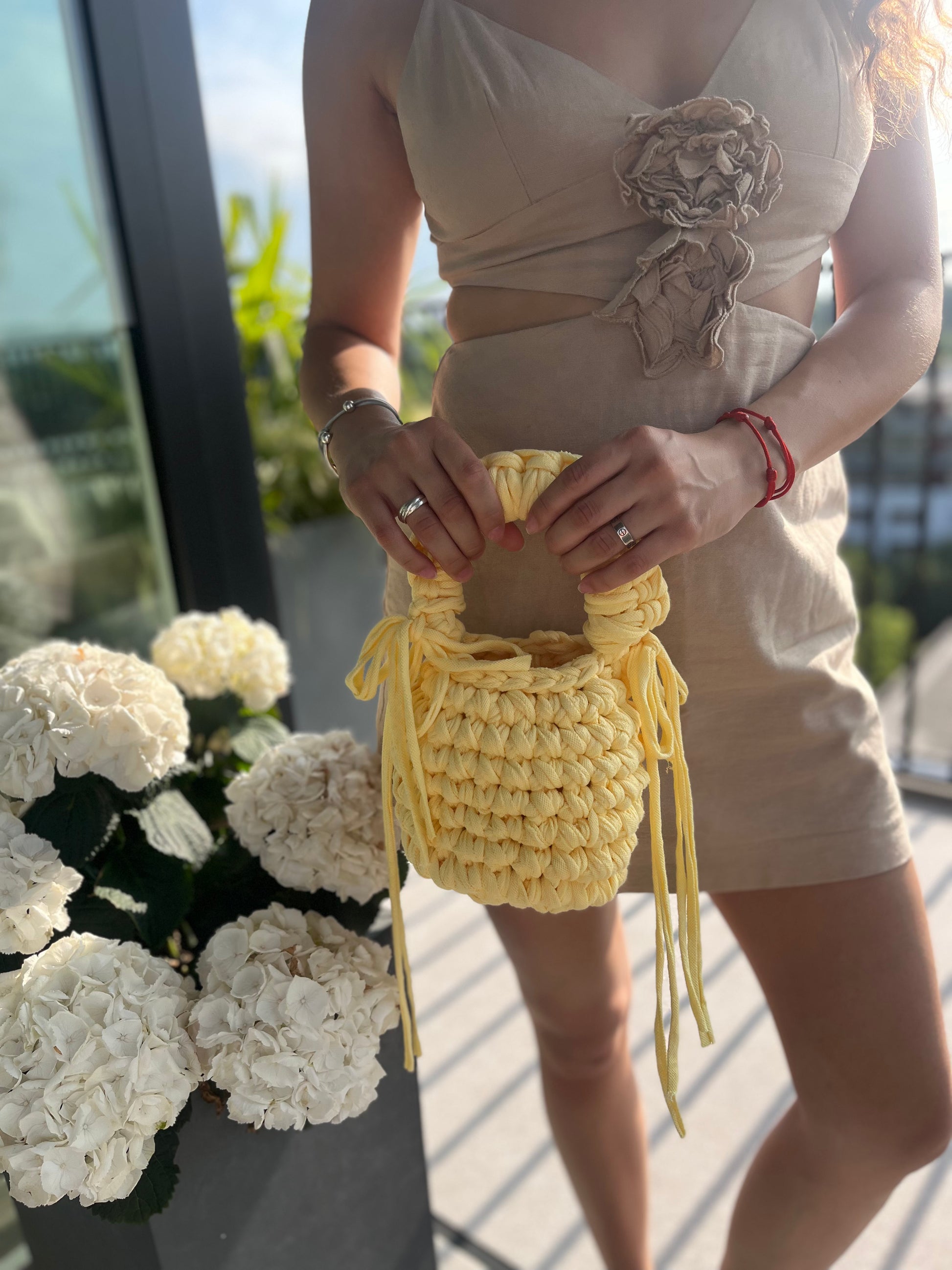Person holding a yellow crochet bag with white flowers in the foreground