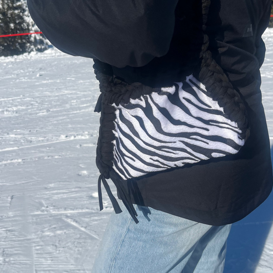 Person wearing a black jacket with a zebra-patterned pouch on a snowy landscape