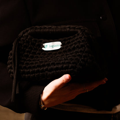 Person holding a black textured pouch with a visible brand label.