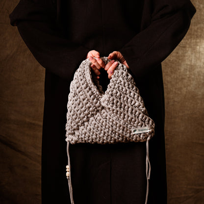 Person holding a textured gray bag against a brown background