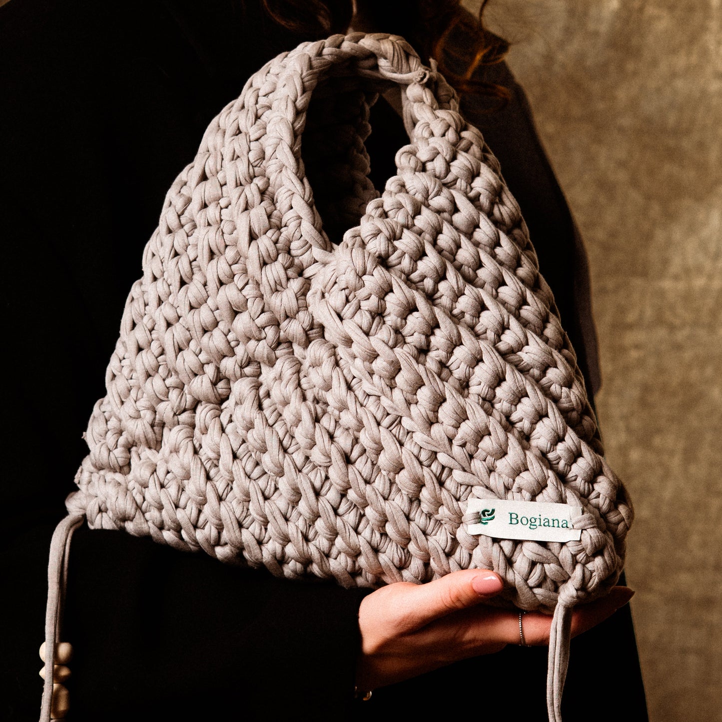 Person holding a textured handbag with a visible brand label against a dark background
